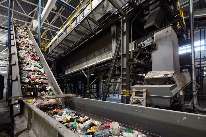 Conveyor belt at recycling plant transports garbage inside drum filter or rotating cylindrical sieve with trommel or screen for sorting pieces of garbage into various sizes fractions